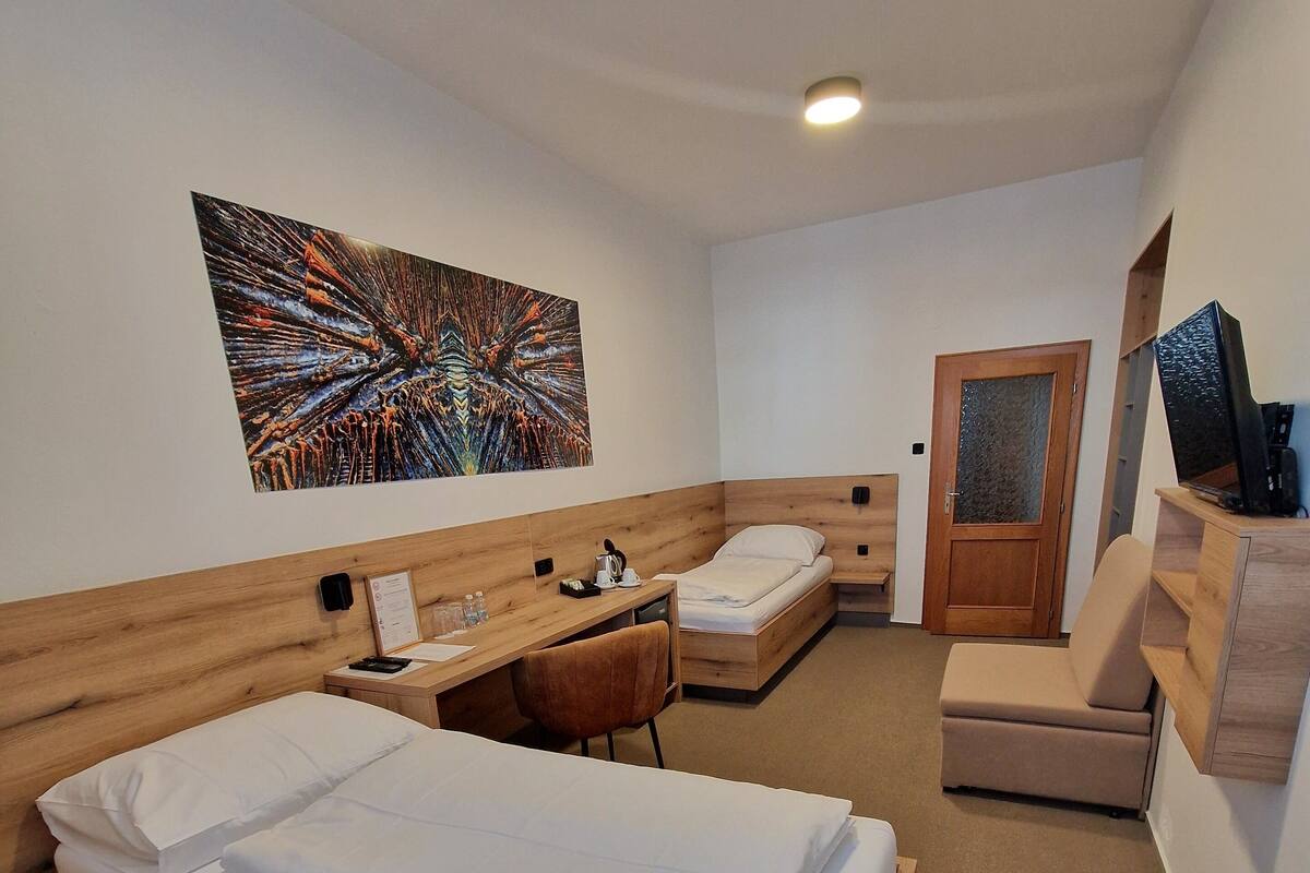 Ein Hotelzimmer mit zwei Holzbetten, einem Schreibtisch, einem Sessel, einer Couch und einem Fernseher.