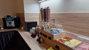 Zona de buffet con una máquina de café, diferentes alimentos y una exhibición de frutas.