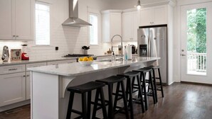 A modern kitchen with white cabinetry, a large island with bar stools, stainless steel appliances, and a view to the outdoors. - NEW The Icon House, East Nashville (Nashville)