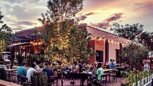 An outdoor dining area with brick walls and string lights, surrounded by greenery. - NEW The Icon House, East Nashville (Nashville)