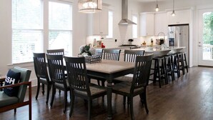 A modern kitchen with white cabinetry, a central island with stools, and a dining table with chairs. - NEW The Icon House, East Nashville (Nashville)