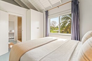 A bedroom with a large bed, a window with curtains, a wardrobe, and a view of palm trees outside. - Beachfront Family vacation Home with private chef and housekeeping - privacy ! (Placencia village)