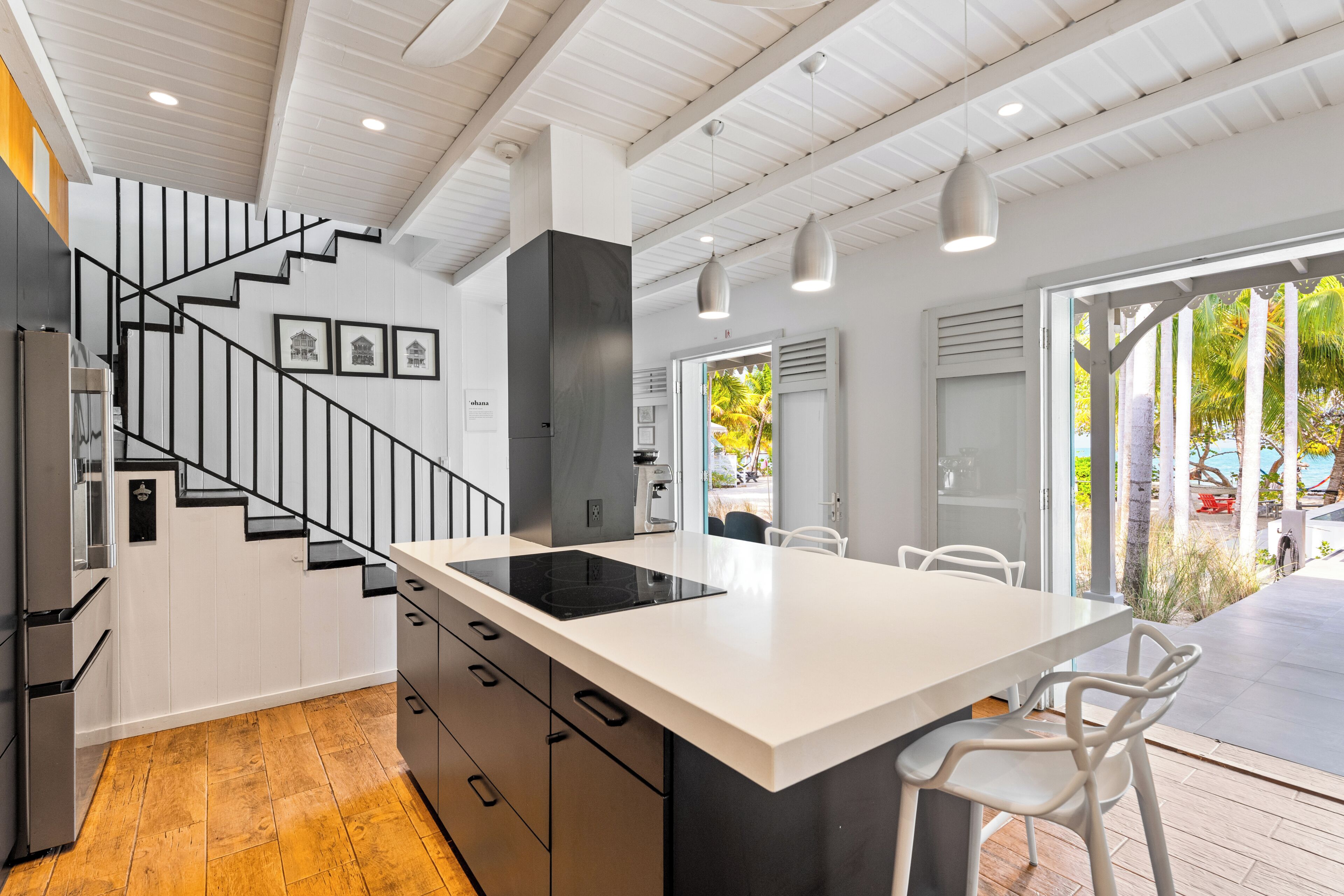A modern kitchen with a central island, black staircase, and a view of the outdoors.
