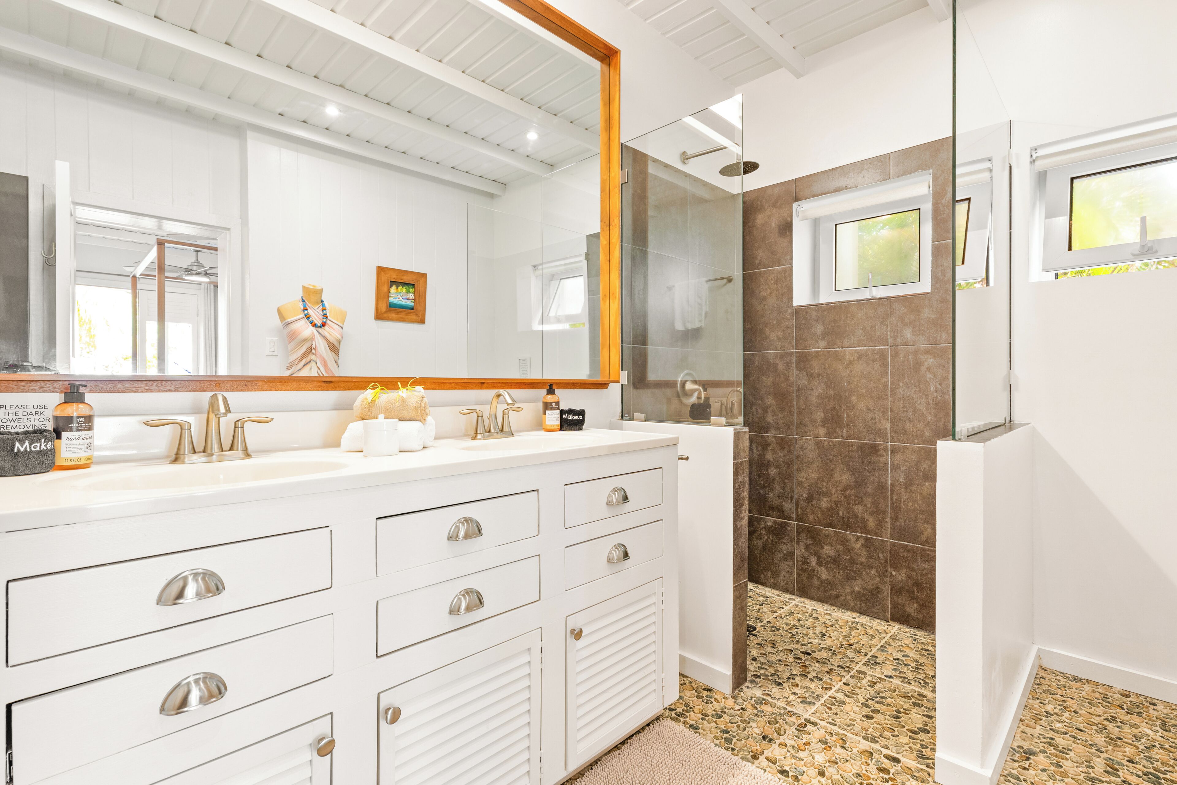 A modern bathroom with a large mirror, white vanity, and a shower area.
