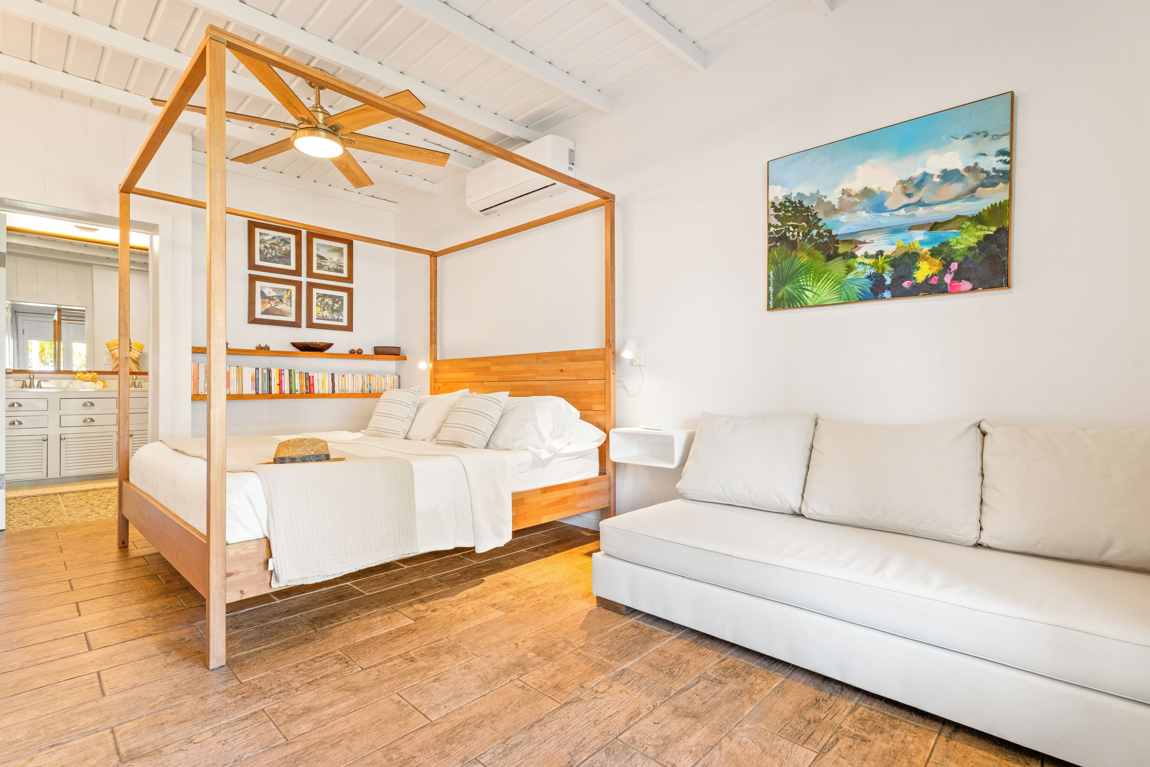 A bedroom with a four-poster bed, a white sofa, a bookshelf, and a painting on the wall.
