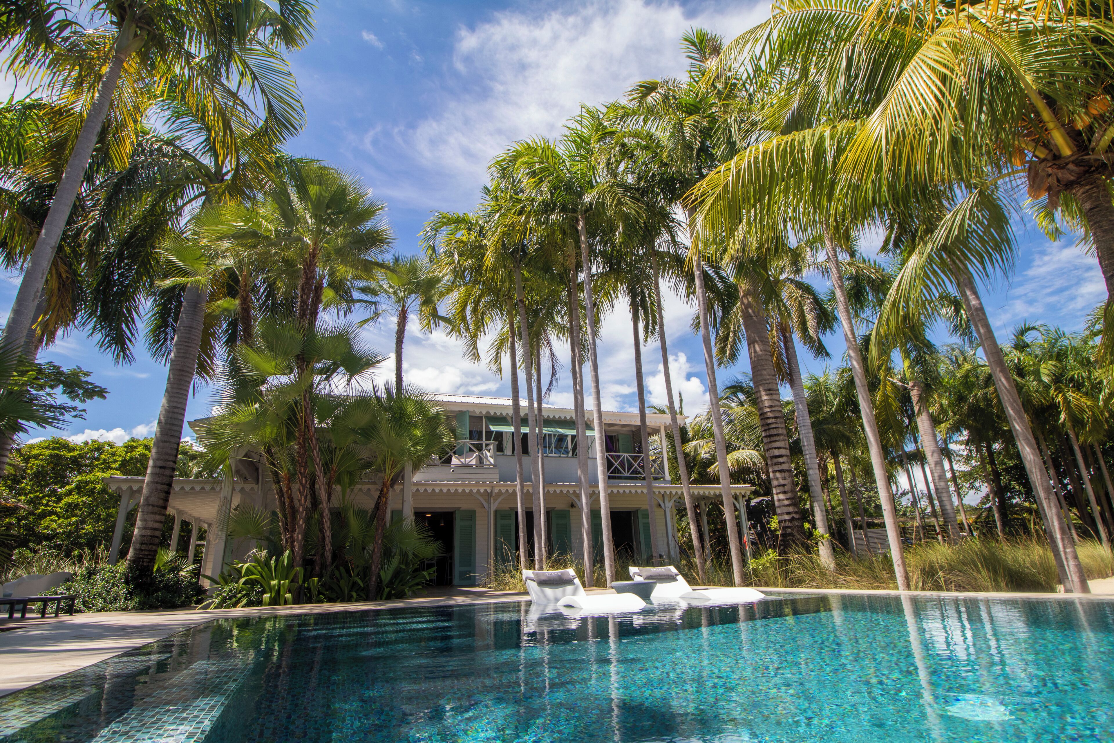 A pool with lounge chairs, surrounded by tall palm trees and a building with a balcony.