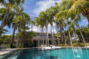 A pool with lounge chairs, surrounded by tall palm trees and a building with a balcony.