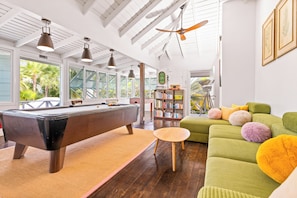 Um quarto amplo com mesa de bilhar, sofá verde e estante de livros.