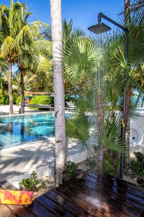 A pool area with a wooden deck, palm trees, and a showerhead.