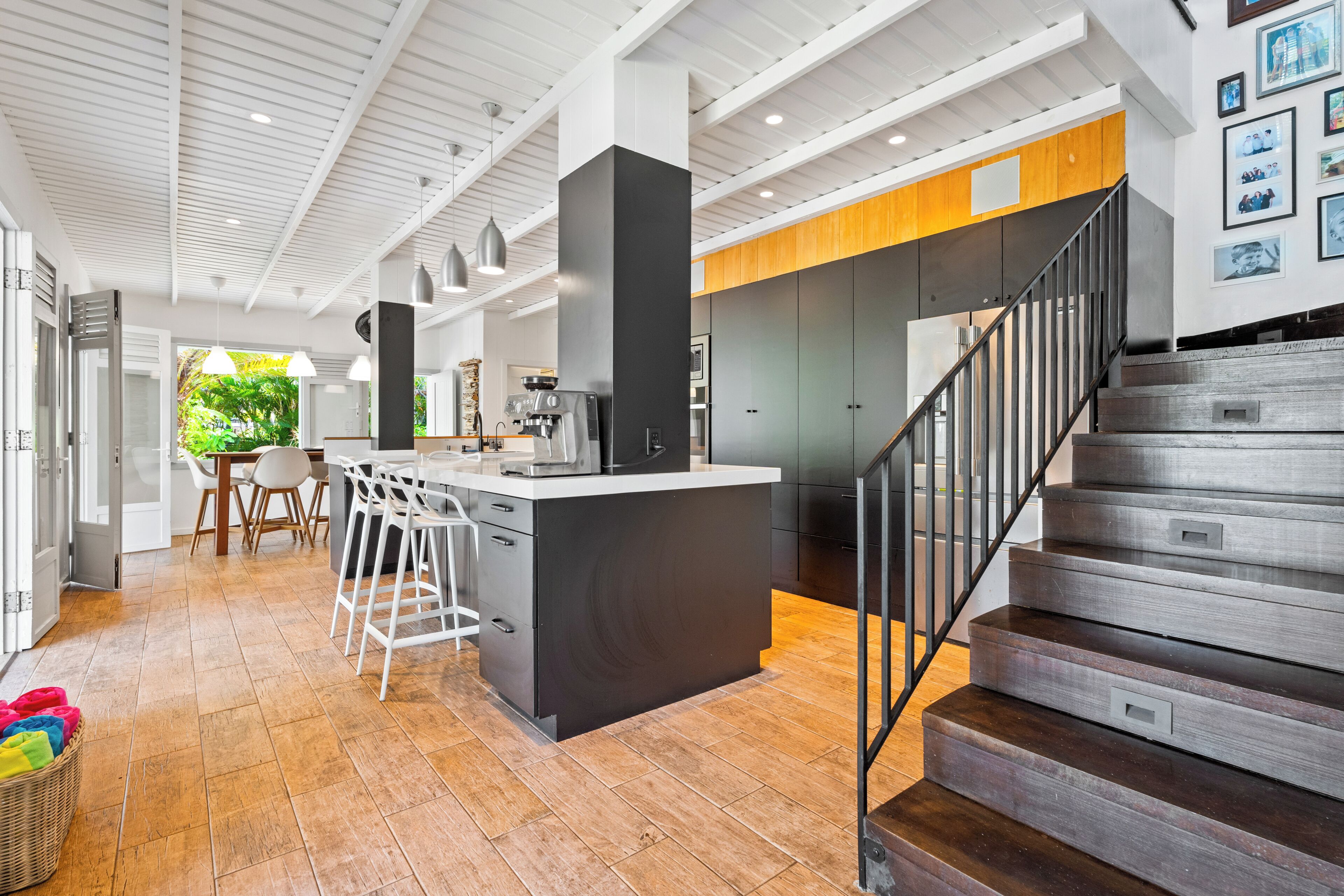 A modern kitchen with a central island, a dining area with bar stools, and a staircase leading to an upper level.