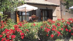 A house with a tiled roof, a patio with a table and chairs, and a garden with red flowers. - Agriturismo Il Casalino (Spoleto)
