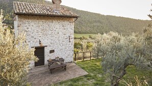 A stone building with a tiled roof, a wooden bench, and a table with flowers. - Agriturismo Il Casalino (Spoleto)