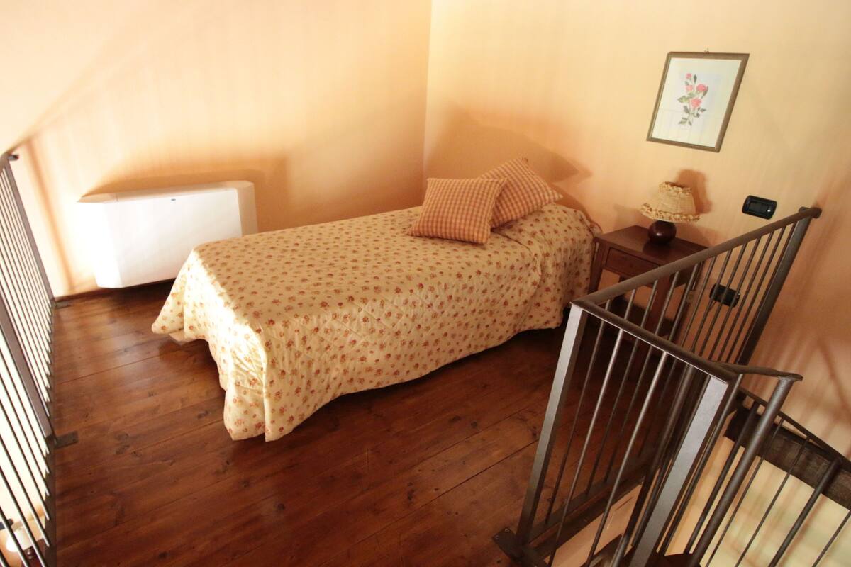 Ein kleines Schlafzimmer mit einem Einzelbett, einem Nachttisch, einer Lampe und einem gerahmten Bild an der Wand.