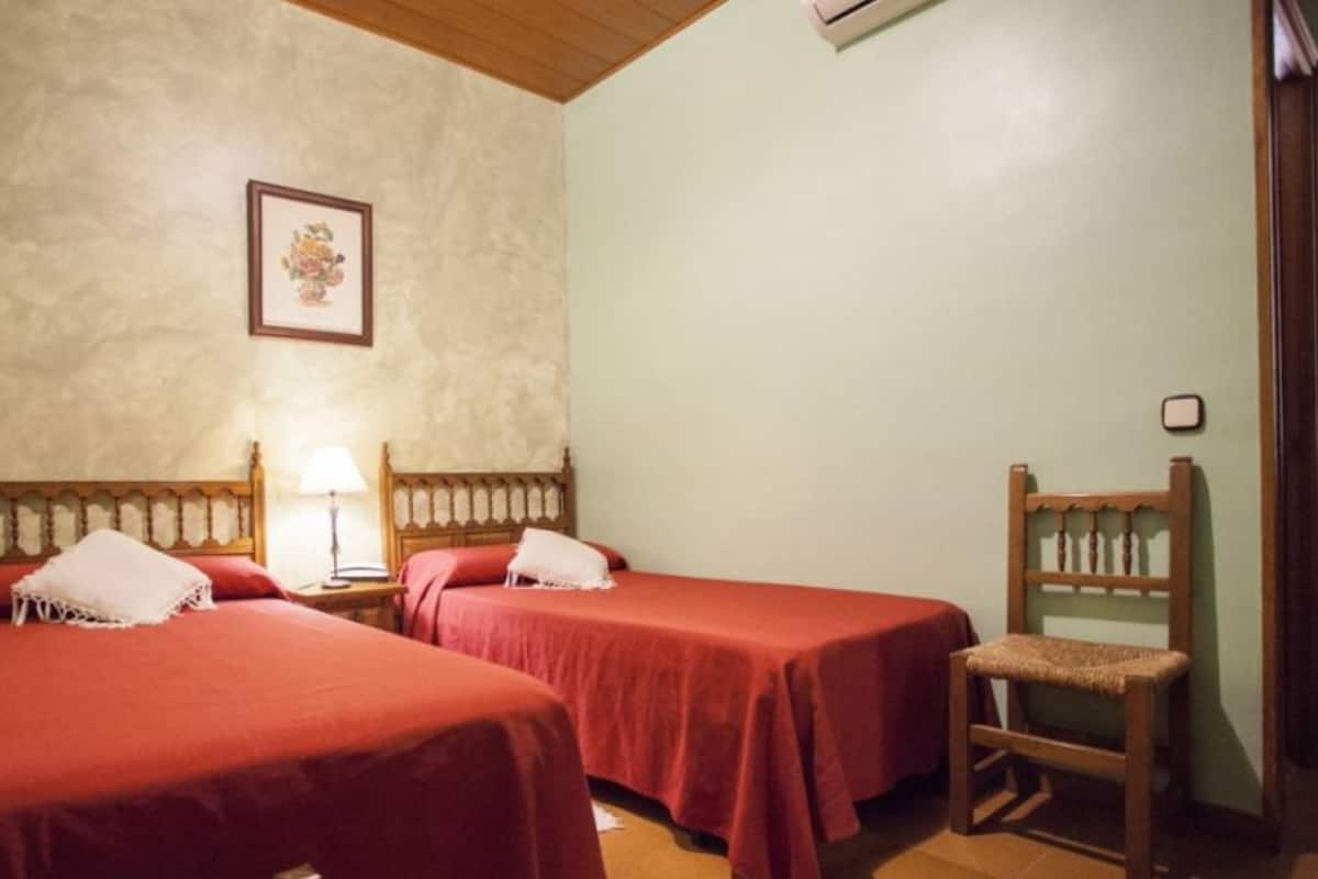 A room with two beds, a wooden chair, a nightstand with a lamp, and a framed picture on the wall.