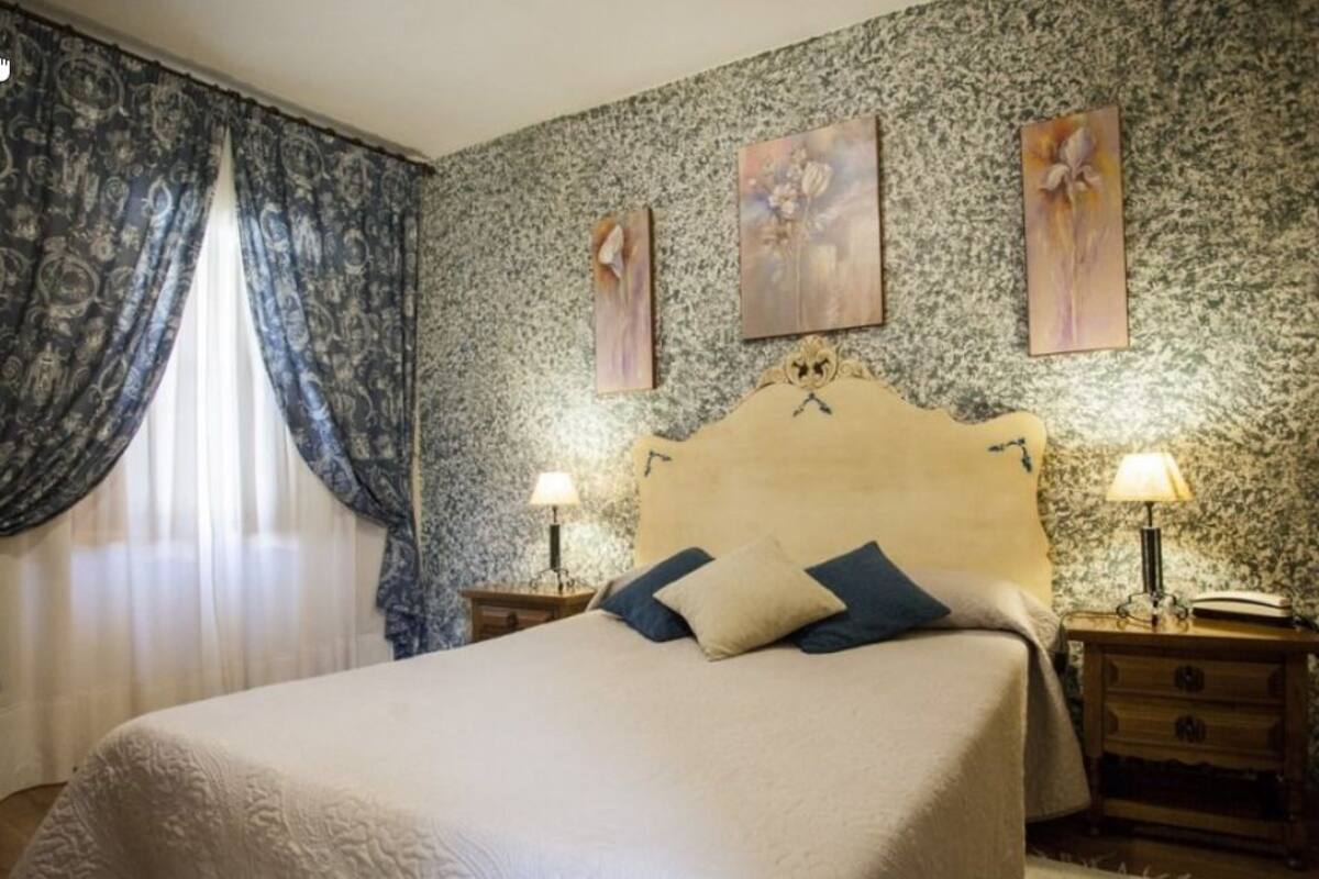 A bedroom with a large bed, two bedside tables with lamps, and floral artwork on the wall.