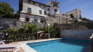 A swimming pool with a stone wall and a building with arched windows in the background. - Hostal Chinchon (Chinchon)