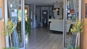 Entrada de hotel con suelo de baldosas, un mostrador de recepción y plantas en macetas.