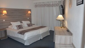 Una habitación de hotel con cama, dos lámparas de noche, televisión y escritorio con lámpara.