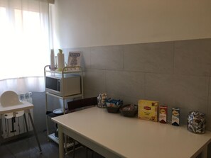 Eine Küchenzeile mit einer Mikrowelle, einem Hinweisschild, einem Hochstuhl und verschiedenen Lebensmitteln auf der Arbeitsfläche.