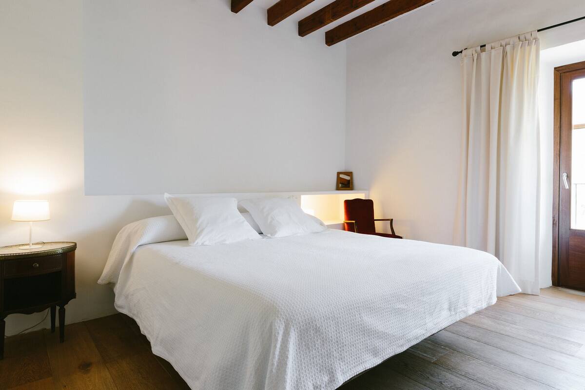 A neatly made bed with white linens in a room with wooden flooring and a simple, clean design.
