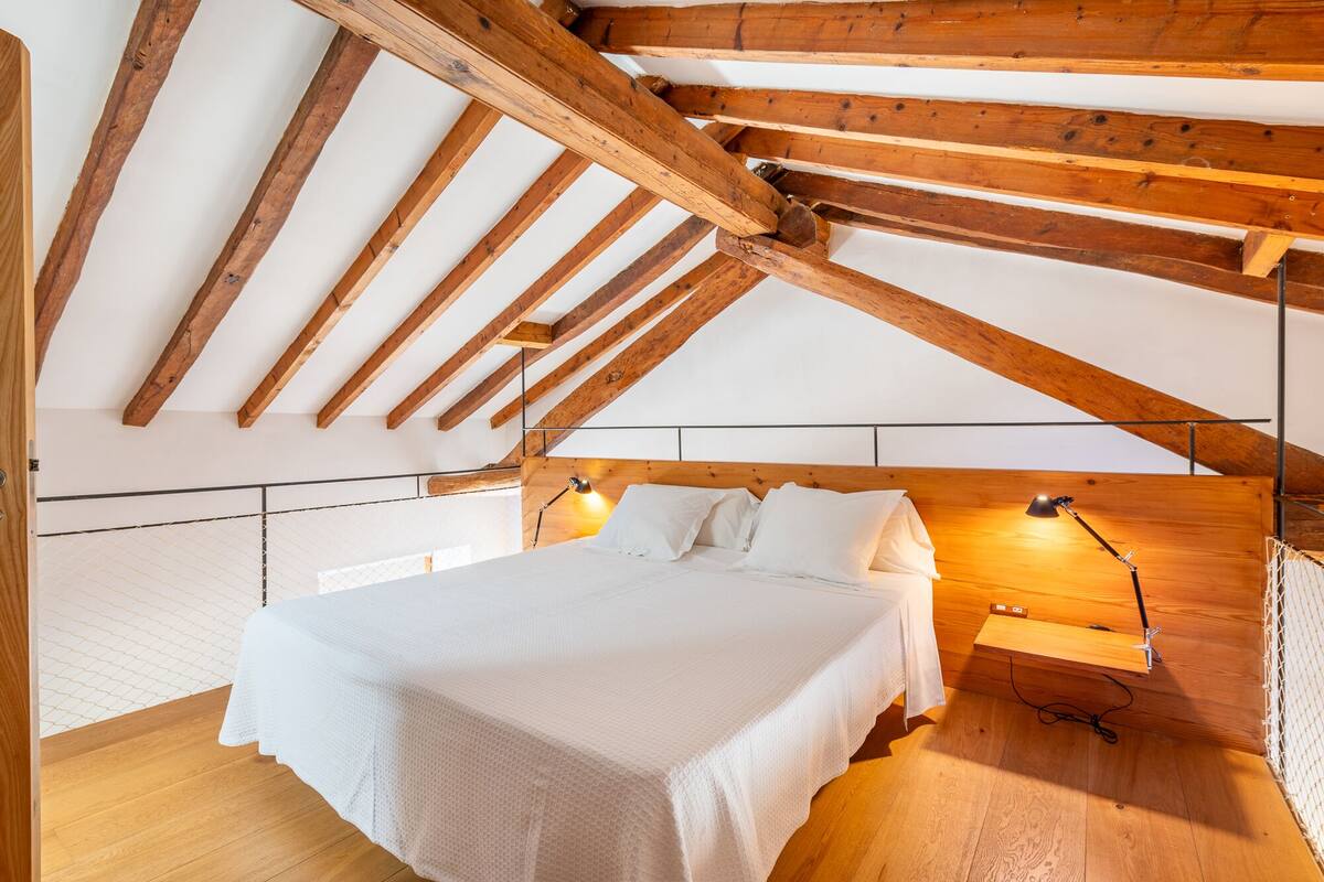 A bedroom with a wooden ceiling, a bed with white bedding, and two bedside lamps.