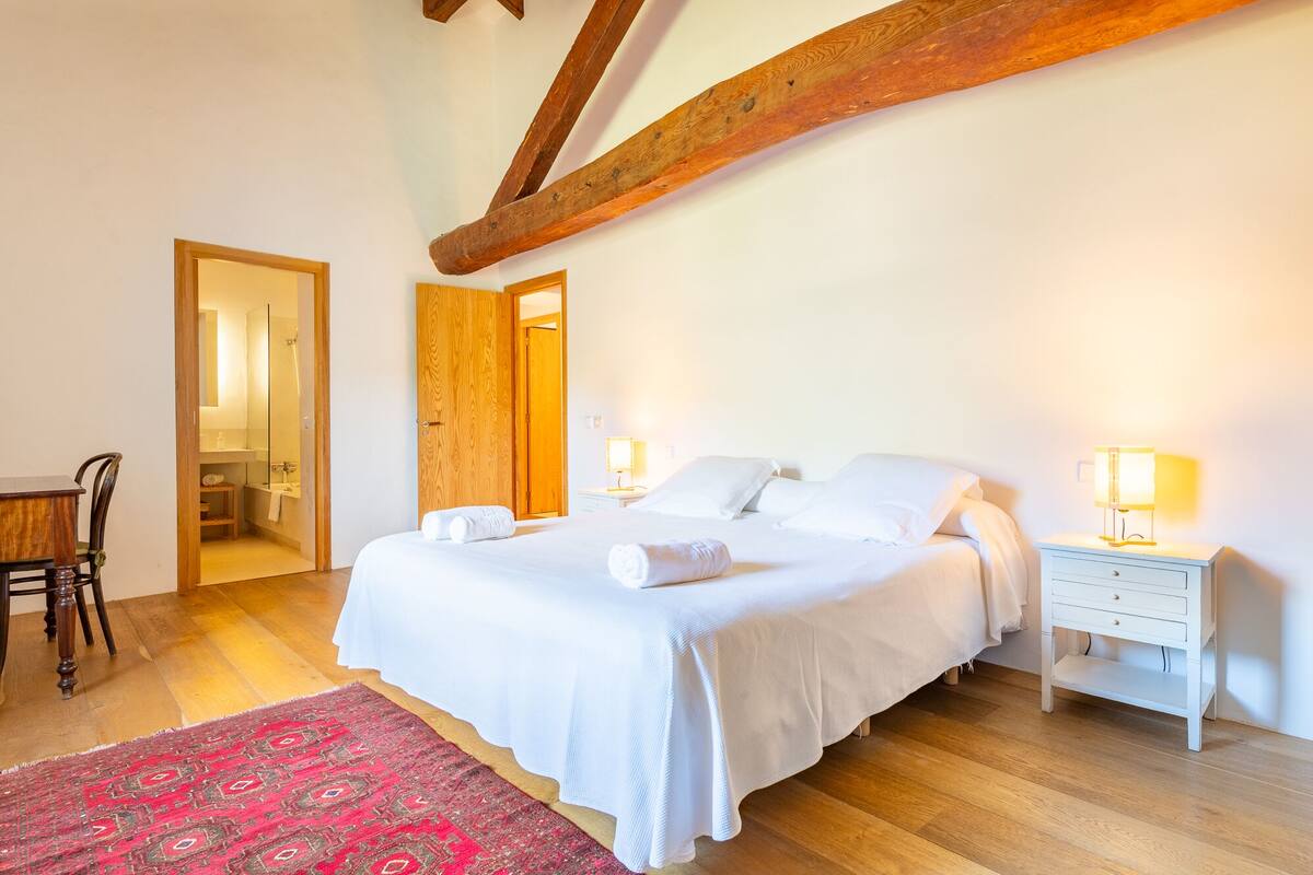 A bedroom with a bed, bedside tables, a chair, and a red patterned rug.