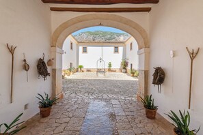 An arched entrance to a building with a cobblestone courtyard, potted plants, and rustic tools on the walls. - Agroturismo Filicumis (Lloseta)