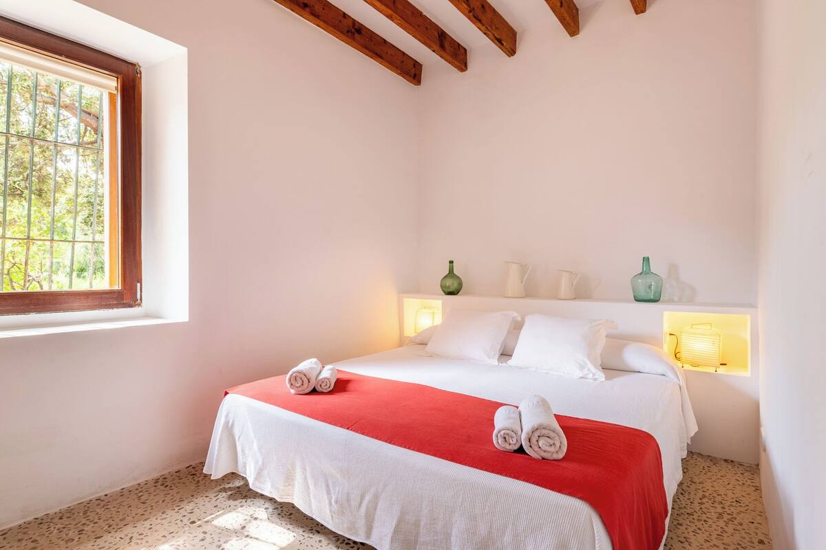 A bedroom with a bed, a window, and a shelf with decorative items.