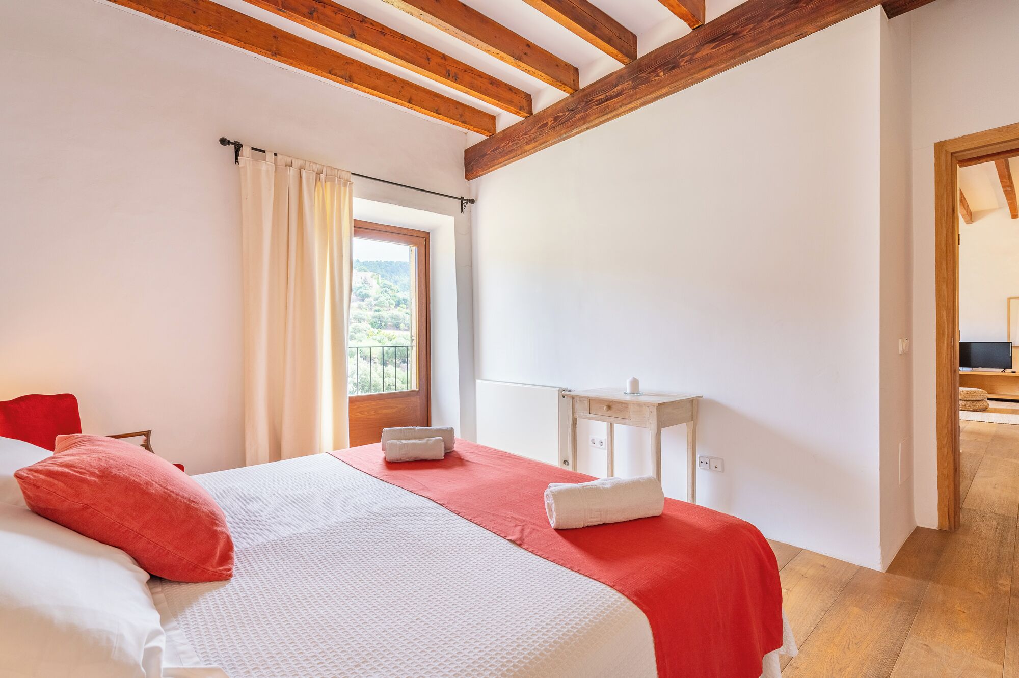 A bedroom with a bed, a nightstand, a window with curtains, and a view of greenery outside.