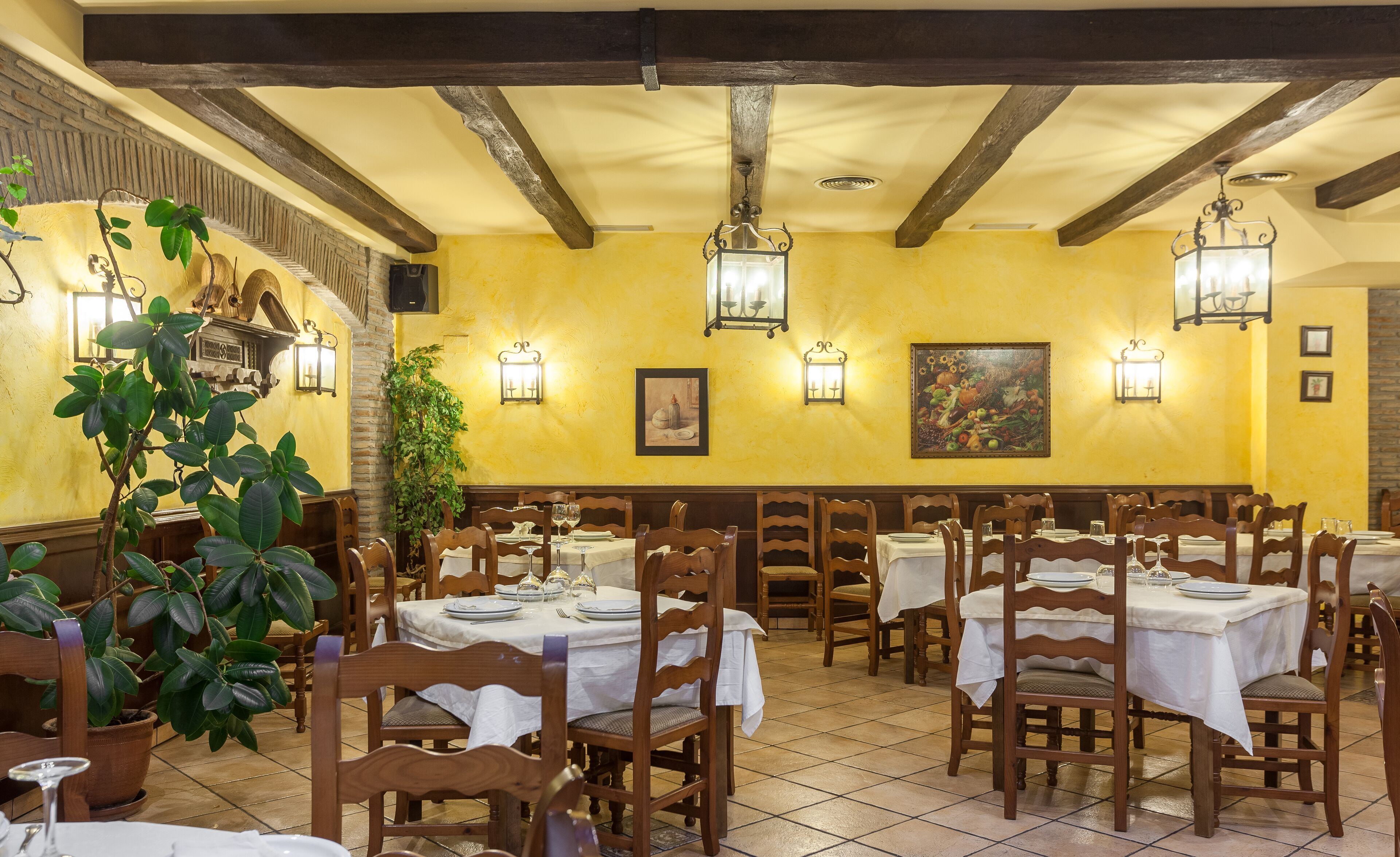 A restaurant with wooden tables and chairs, yellow walls, and hanging lanterns.