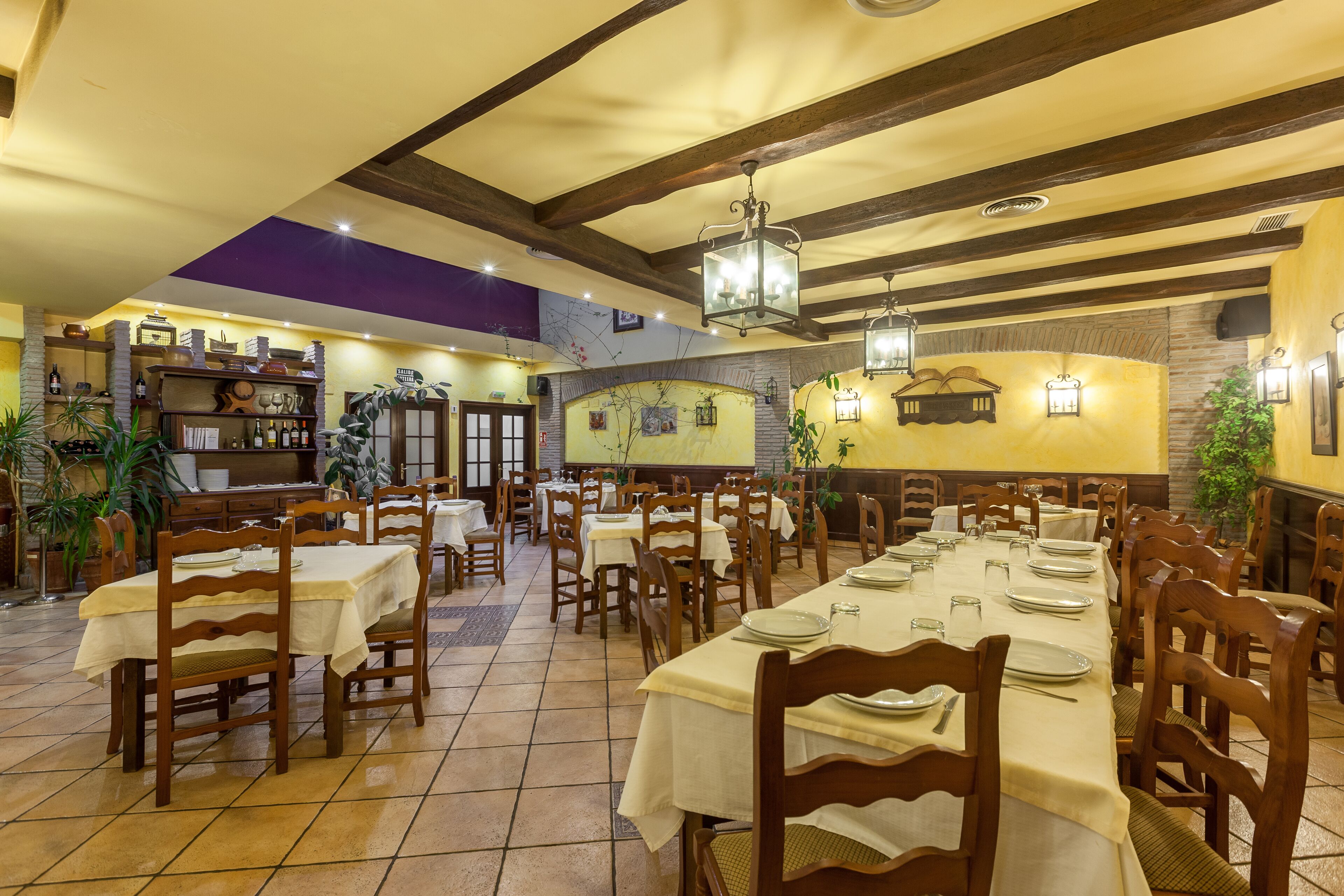 A restaurant with wooden tables and chairs, a bar area, and a tiled floor.