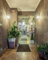 Entrada de hotel con un cartel que dice "Hotelia", una recepción y plantas en macetas.
