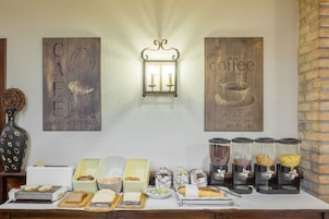 Montaje de un bufé de desayuno con diversas opciones de comida y una estación de café, que incluye un cartel anunciando café y un espejo.