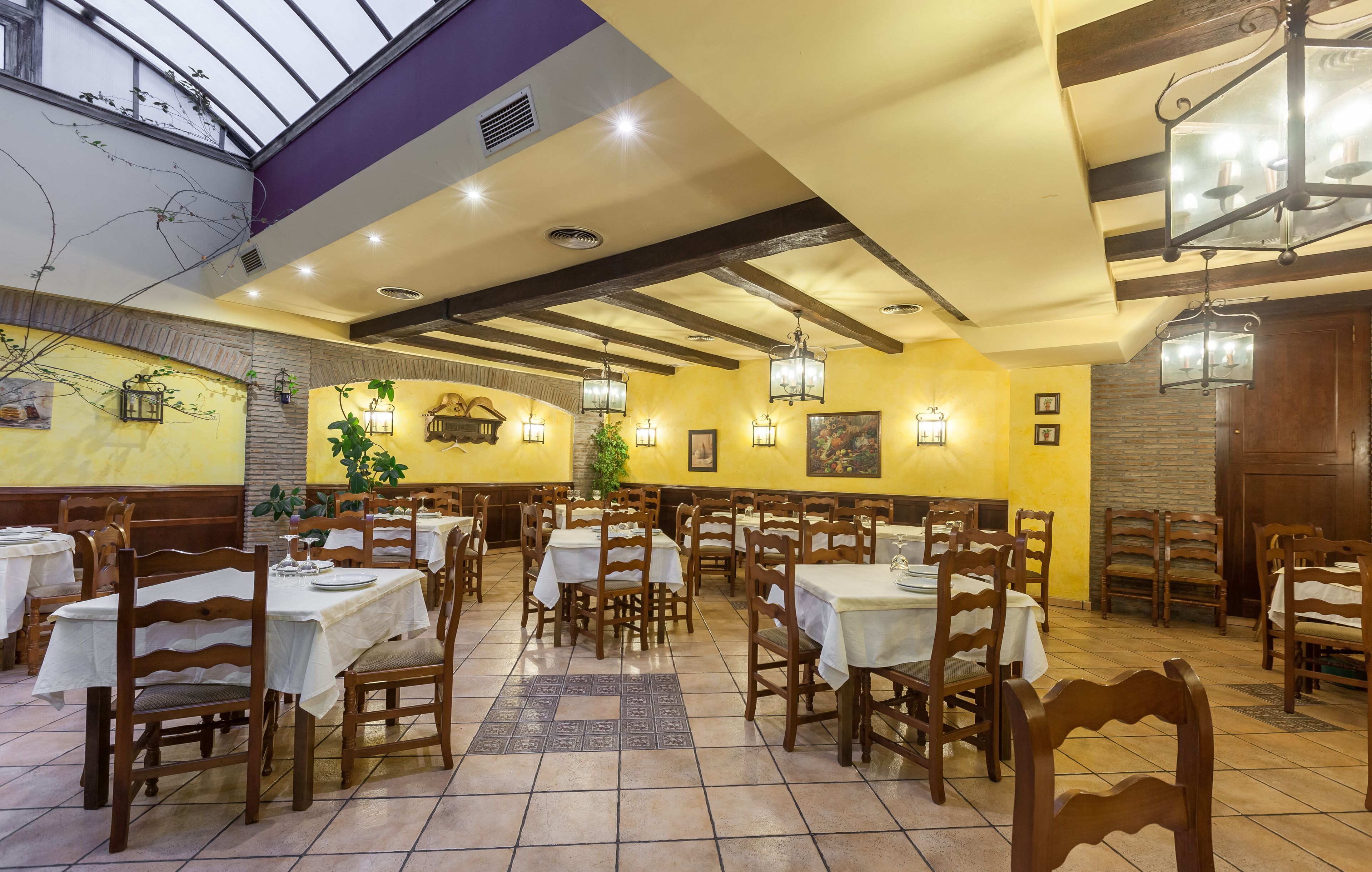 Ein Restaurant mit mehreren Tischen und Stühlen, einer hohen Decke mit freiliegenden Balken und Wandleuchten.