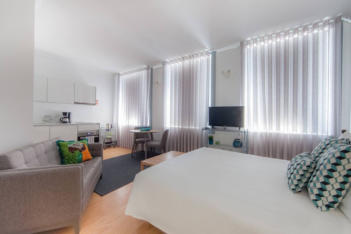 A hotel room with a bed, a sofa, a desk with a chair, a TV, and curtains.