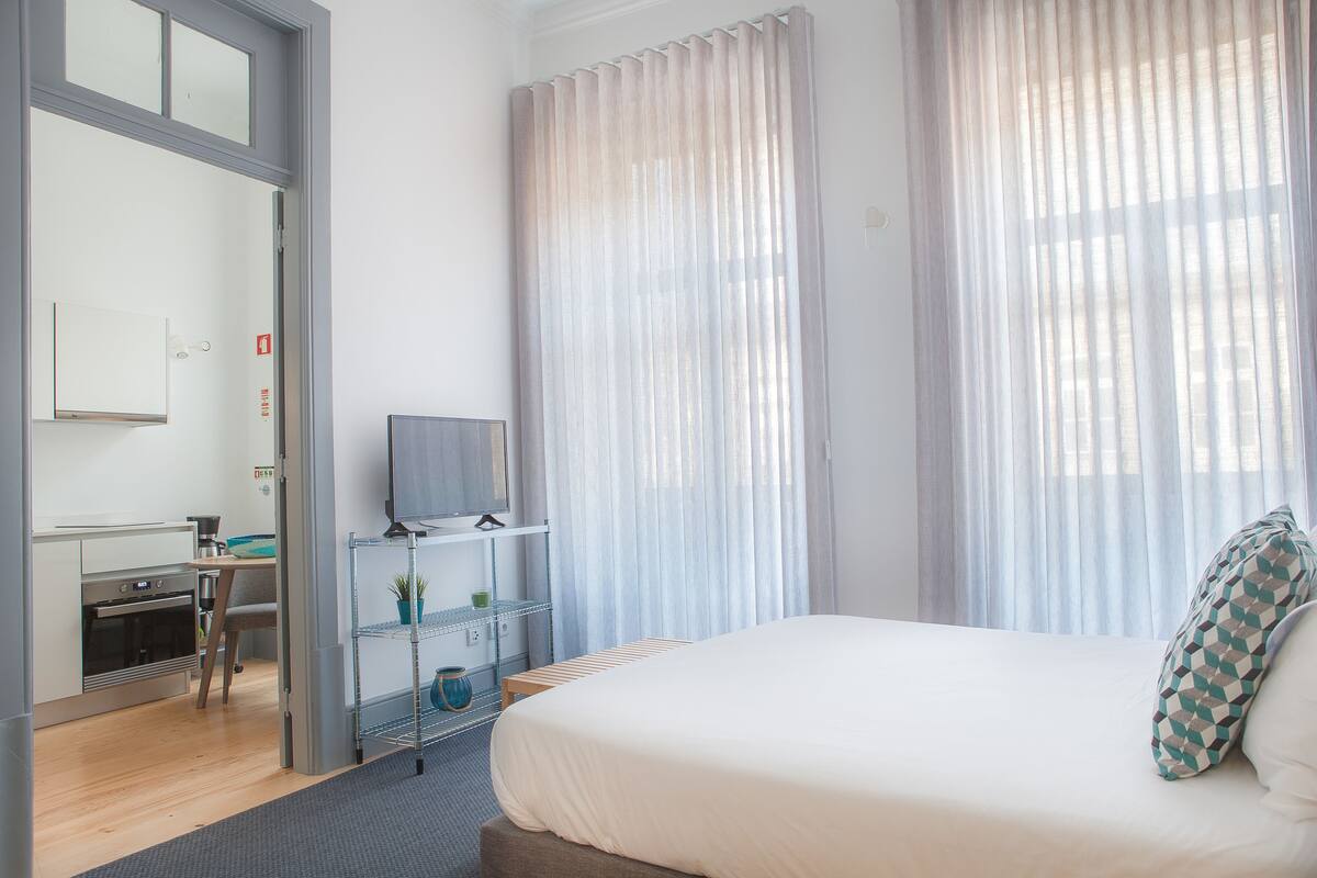 A hotel room with a bed, a TV, a desk, and a kitchenette.