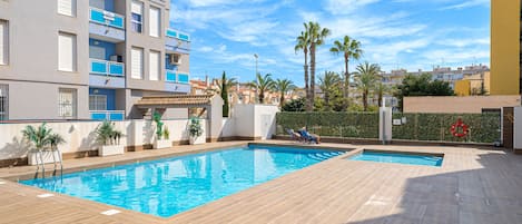 A swimming pool with two sun loungers, a lifebuoy, and a view of a residential area with palm trees.