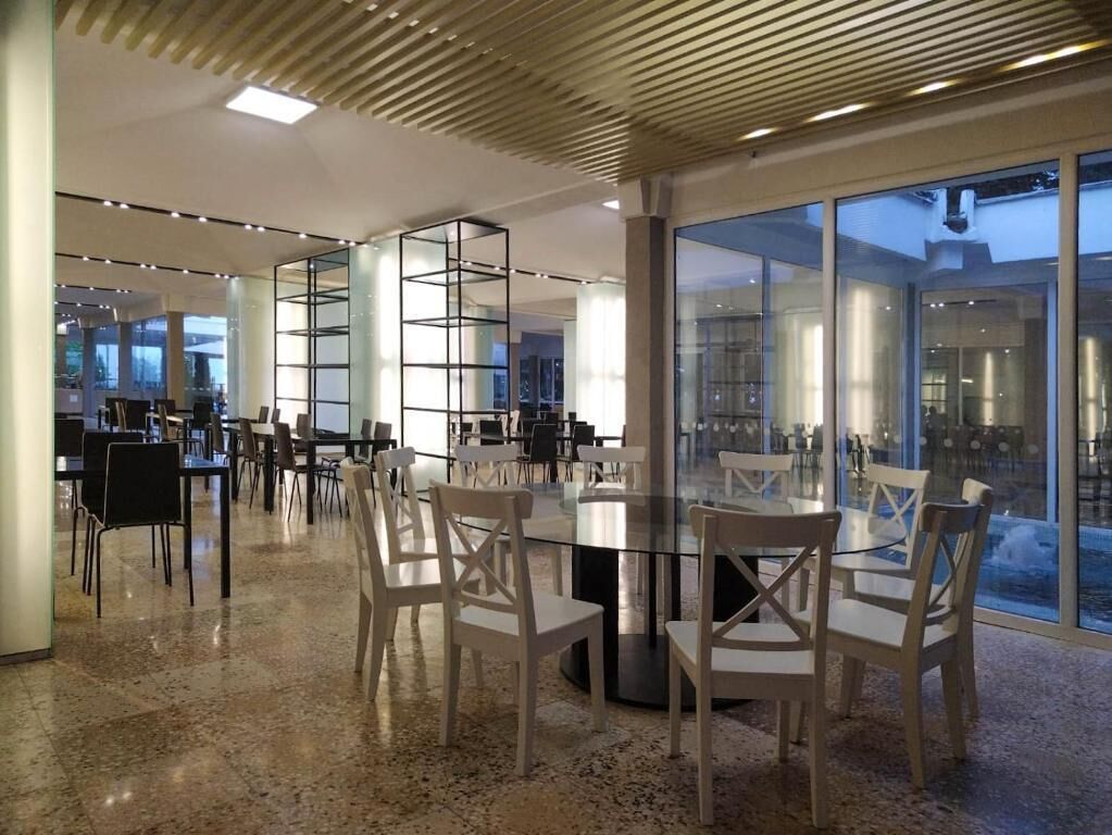 Ein modernes Interieur mit einem runden Glastisch, umgeben von Stühlen, einer Holzbalkendecke und großen Fenstern.
