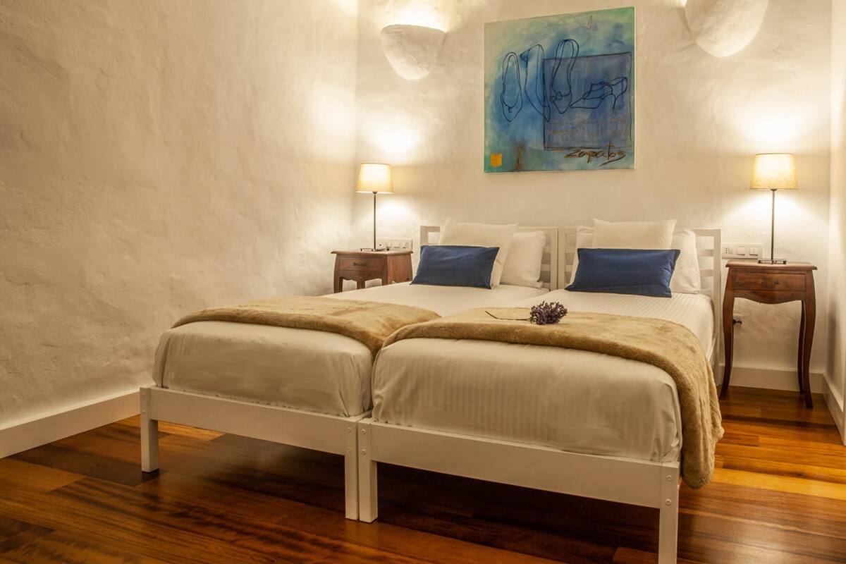 A bedroom with a white bed, two bedside tables, and a painting on the wall.
