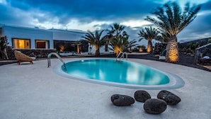 Ein Swimmingpool mit Steinrand, Palmen und einem modernen Gebäude im Hintergrund.