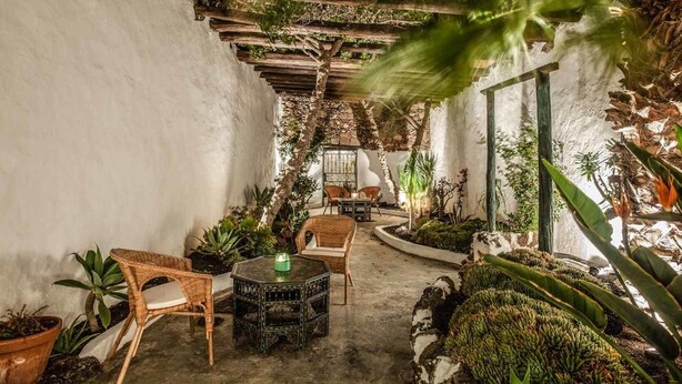 Ein gemütlicher Innenhofgarten mit einer Holzpergola, einer Sitzgruppe und verschiedenen Blumentöpfen.