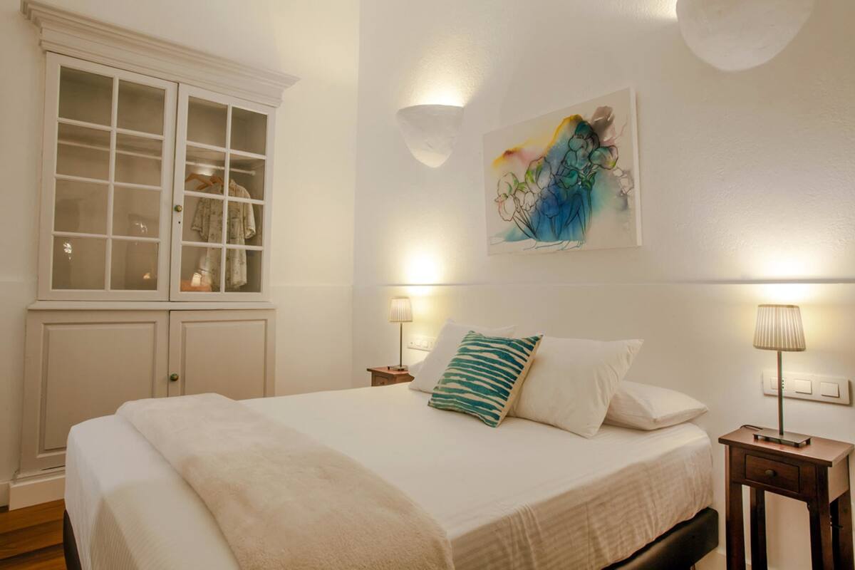 A bedroom with a large bed, a wardrobe, a painting on the wall, and two bedside lamps.