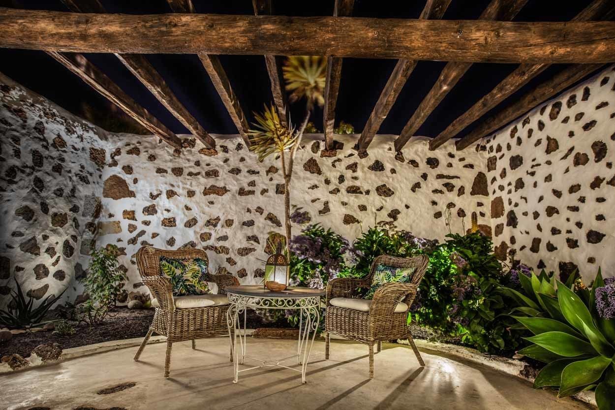 Um pátio externo com paredes de pedra, móveis de vime e plantas em vasos.