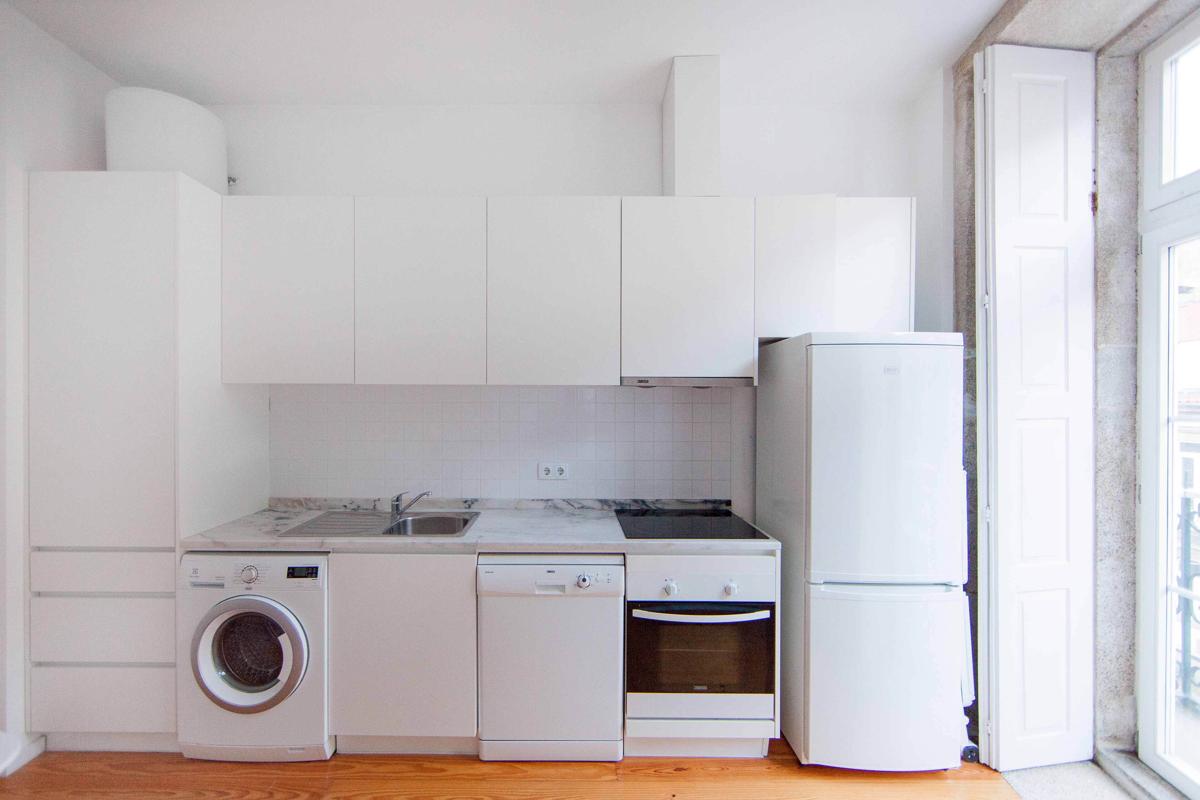 Una cocina compacta con armarios blancos, lavadora integrada, lavavajillas y refrigerador.