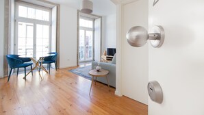 Un salon moderne avec un plancher en bois, un canapé, deux fauteuils bleus, une petite table ronde et une porte portant le numéro « 2 ».