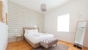Une chambre à coucher avec un lit, une table de chevet, un miroir et un mur orné d’un motif géométrique.