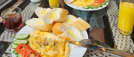 Une table mise pour le petit-déjeuner, avec des assiettes d’œufs, du pain et des légumes, ainsi que des verres de jus d’orange.