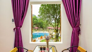 A room with a window view of a pool, two wicker chairs, a small table with a vase and two cups, and purple curtains. - Tam Coc Lavender Homestay (Nam Hoa Lu)