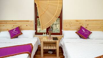 Hotellihuone, jossa on kaksi sänkyä, ja jokaisessa sängyssä on violetti tyyny, jossa on merkintä ”Lavender Homestay”. Huoneessa on myös puinen yöpöytä, jossa on maljakko ja pulloja, sekä ikkuna, jossa on bambusta valmistettu sälekaihdin.