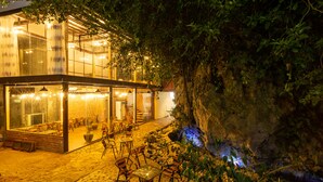 An outdoor dining area with tables and chairs, a glass enclosure, and a view of a cave-like structure. - Tam Coc Lavender Homestay (Nam Hoa Lu)